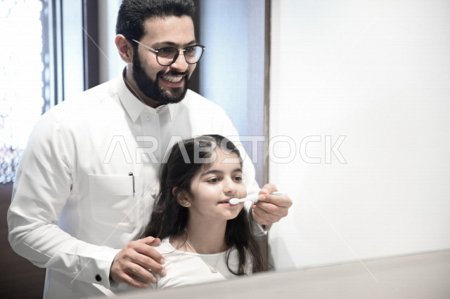 رجل عربي خليجي سعودي يساعد ابنته في تنظيف اسنانها والعناية بها ،تجنب تسوس الاسنان وامراض اللثة ، النظافة الشخصية والاهتمام بالنفس ، الرعاية الصحية للاطفال