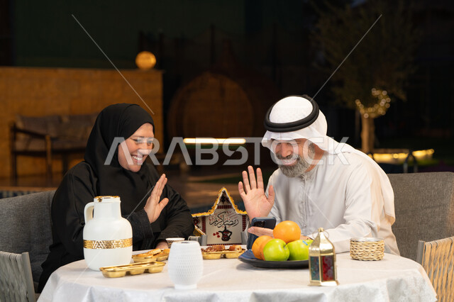 استخدام الوسائل التقنية الحديثة، قضاء وقت ممتع في جلسة خارجية في احدى الشاليهات، زينة وديكور المناسبات والأعياد الاسلامية، أجواء عائلية سعيدة في شهر رمضان المبارك، زوجان عربيان خليجيان اماراتيان يقومان بإجراء مكالمة فيديو بإيماءات السعادة والسرور