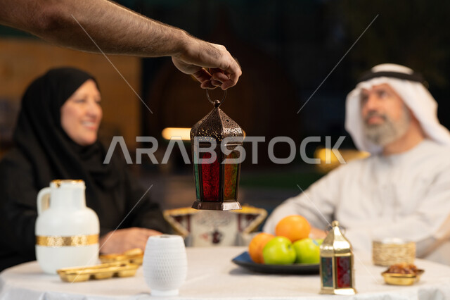 ديكورات وزينة المناسبات والأعياد الاسلامية، تبادل الأحاديث والتسامر بين الأفراد، صورة مقربة ليد رجل يحمل فانوس معدني مضيء، أسرة عربية خليجية اماراتية تقضي أوقات ممتعة في جلسة خارجية في احدى الشاليهات، أجواء عائلية سعيدة في شهر رمضان المبارك