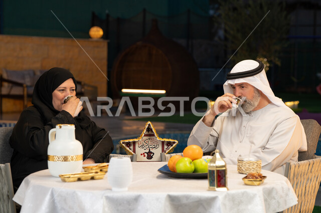 الجلوس في الخارج في احدى الشاليهات الراقية، قضاء أوقات ممتعة في الهواء الطلق، ديكورات وزينة المناسبات والأعياد الاسلامية، أجواء عائلية سعيدة في شهر رمضان المبارك، زوجان عربيان خليجيان إماراتيان يقومان بتناول القهوة العربية