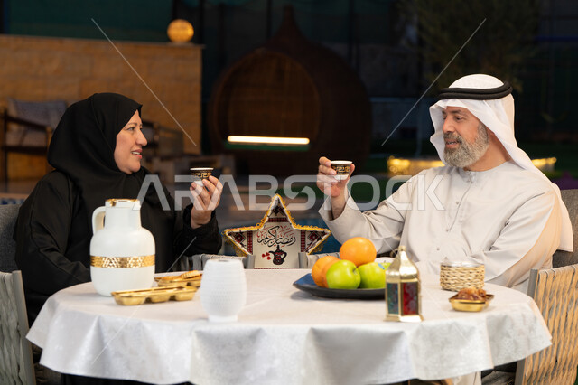 شرب القهوة الساخنة بعد الافطار، ديكورات وزينة المناسبات والأعياد الاسلامية، أجواء عائلية سعيدة في شهر رمضان المبارك، زوجان عربيان خليجيان إماراتيان يجلسان في احدى الشاليهات الراقية