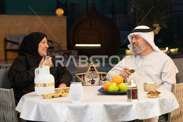 الجلوس في الخارج في احدى الشاليهات الراقية، قضاء أوقات ممتعة في الهواء الطلق، ديكورات وزينة المناسبات والأعياد الاسلامية، أجواء عائلية سعيدة في شهر رمضان المبارك، زوجان عربيان خليجيان إماراتيان يقومان بتناول القهوة العربية