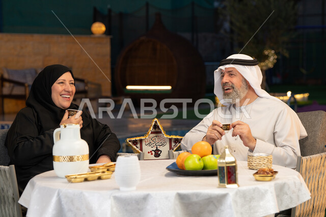 شرب القهوة الساخنة بعد الافطار، ديكورات وزينة المناسبات والأعياد الاسلامية، أجواء عائلية سعيدة في شهر رمضان المبارك، زوجان عربيان خليجيان إماراتيان يجلسان في احدى الشاليهات الراقية