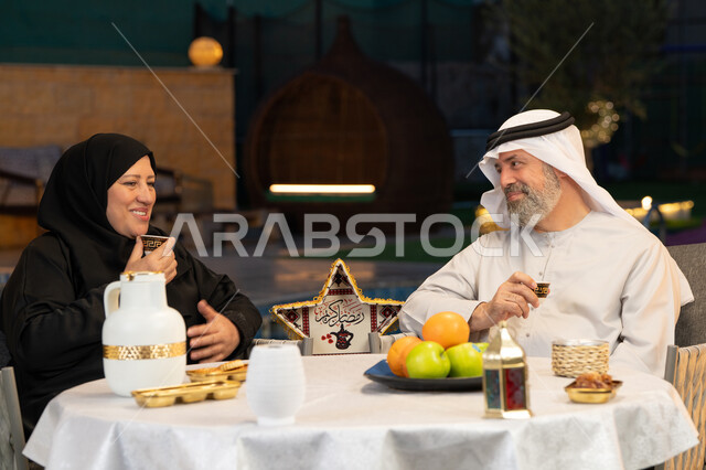 الجلوس في الخارج في احدى الشاليهات الراقية، قضاء أوقات ممتعة في الهواء الطلق، ديكورات وزينة المناسبات والأعياد الاسلامية، أجواء عائلية سعيدة في شهر رمضان المبارك، زوجان عربيان خليجيان إماراتيان يقومان بتناول القهوة العربية