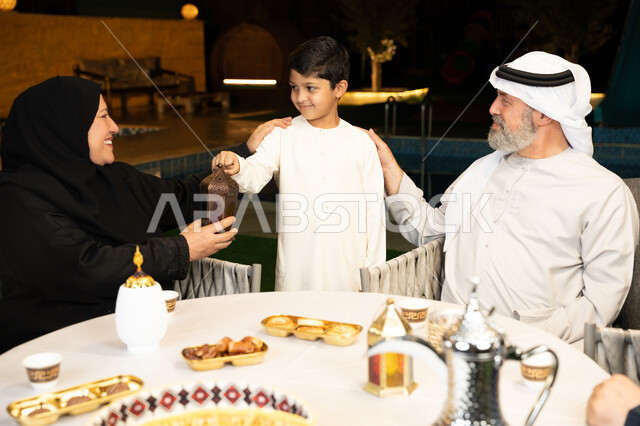 Grandparents' affection for their grandchildren, gestures of happiness and pleasure at a family gathering, various and delicious Ramadan sweets, decorations for Islamic occasions and holidays, an Emirati Gulf Arab family spending a pleasant time in an outdoor session in one of the chalets, a boy holding a lit metal lantern in his hand