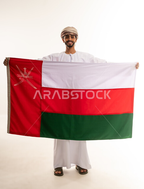 Pride and pride in national identity, national cultures and symbols, national flag of the country, portrait of a smiling Omani Gulf Arab man wearing a dishdasha and turban celebrating National Day, full body, white background