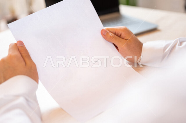 رجل عربي خليجي سعودي يجلس امام الحاسوب المحمول، أوراق بيضاء فارغة، سكرتير يدير الأعمال الورقية، اعمال مكتبية