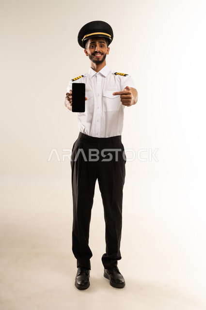 Blank black screen on mobile phone, Saudi Airlines, passenger reception and welcome crew, aviation work, portrait of a smiling Arab Omani Gulf captain in uniform looking at the camera with an expression of happiness and pleasure, full body, white background