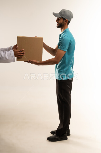 Delivery service and express delivery of orders, delivering goods and orders to customers, smiling Arab Gulf Omani worker wearing casual clothes holding a cardboard box in his hand, Saudi man delivering the order to the customer with expressions of pleasure and satisfaction, full body, white background