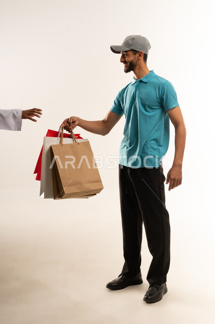 Safe delivery service, online delivery networks in the Gulf, portrait of a young Arab Gulf Omani man wearing casual clothes and a gray hat working as a sales representative, a Saudi man delivering orders, full body, white background