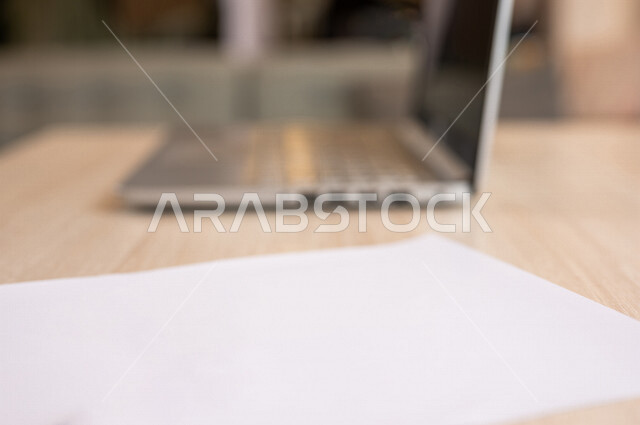 رجل عربي خليجي سعودي يجلس على الحاسوب المحمول وامامه مجموعة من الأوراق الفارغة، ادارة الاعمال من خلال الحاسوب المحمول، ادخال البيانات من خلال لوحة المفاتيح،  محتويات نصية