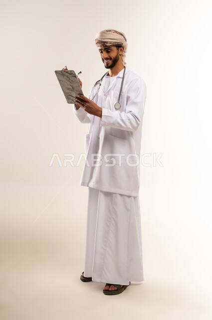 تدوين وتسجيل الوصفة، الفحص الطبي وتقديم الخدمات العلاجية, بورتريه لطبيب عربي خليجي عماني يرتدي الدشداشة والعمامة والمعطف الطبي يضع السماعة الطبية يعمل في العمل في القطاع الصحي في سلطنة عمان، الجسم بالطول الكامل، خلفية بيضاء