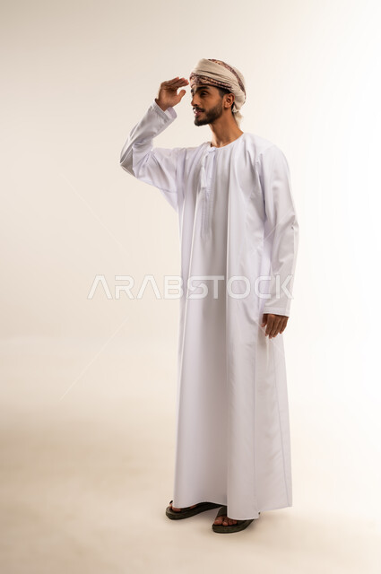Focusing gestures for clear vision, trying to see distant objects, the concept of looking to the future, a portrait of a young Arab man from the Gulf, Omani, wearing a dishdasha and turban, placing his hand on his forehead and looking in a specific direction, full-length body, white background