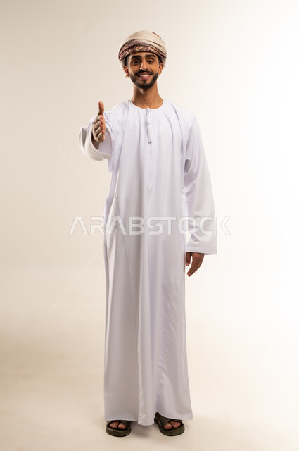Greeting and greeting, acquaintance, friendship and forming social relationships, the concept of reception and welcome, portrait of an Arab Gulf Omani man wearing a dishdasha and turban extending his hand with a handshake expression, full body, white background.