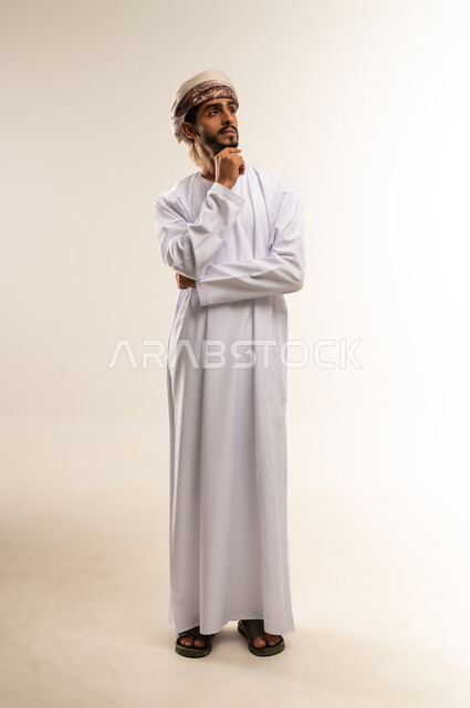 إيماءات محاولة تذكر أمر ما، بورتريه لرجل عربي خليجي عماني يرتدي الدشداشة والعمامة يضع يده على ذقنه ينظر إلى الأعلى بتعابير التفكير، التأمل والتخطيط للمستقبل، التركيز والتمعن لإيجاد حل لمشكلة معينة، الجسم بالطول الكامل، خلفية بيضاء .