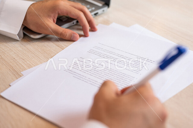 رجل عربي خليجي سعودي يجلس أمام الحاسوب المحمول ويقوم بتوقيع عقد إيجار، قراءة البنود الخاصة بالعقد، التحقق والتدقيق في شروط عقد الايجار، الموافقة على الشروط، التوقيع على العقود