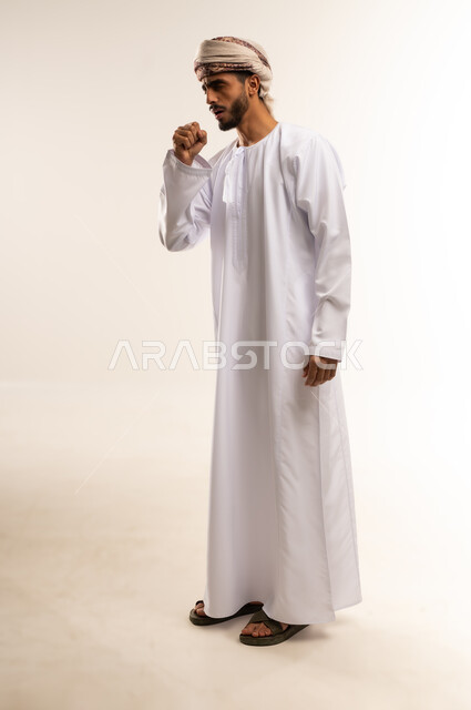 الاصابة بنزلة برد، أعراض فايروس كورونا (كوفيد-19), الحاجة لطلب المساعدة و الذهاب الى الطبيب, بورتريه لرجل عربي خليجي عماني يرتدي الدشداشة والعمامة  يضع يده على فمه بإيماءات السعال و الألم, الشعور بالمرض و التعب والإرهاق, صورة الجسم بالطول الكامل، خلفية بيضاء .