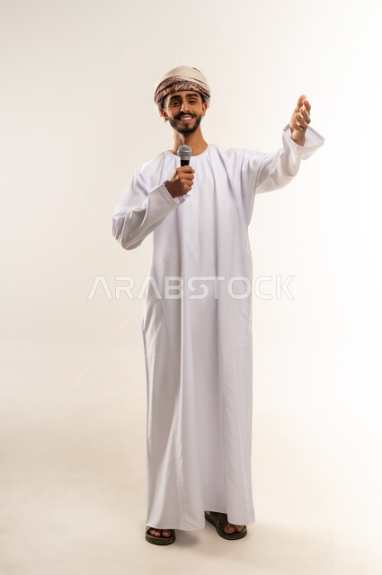 تسجيل مقطع صوتي غنائي, الاستمتاع بممارسة المواهب الفنية، قضاء وقت ممتع بأداء العروض الصوتية، بورتريه لشاب عربي خليجي عماني يرتدي الدشداشة والعمامة يمسك بيده المايكروفون ينظر الى شي ما بايماءات السعادة والسرور, الجسم بالطول الكامل, خلفية بيضاء .