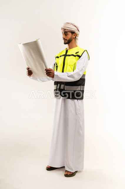 The concept of engineering and architectural construction, looking with gestures of happiness and pleasure, working in the field of engineering, supervising engineering project plans, portrait of an Arab Gulf Omani engineer wearing a dishdasha, a cloak and a protective vest, holding a planner in his hands, professions and jobs for young people in the Sultanate of Oman, full-length body image, white background.