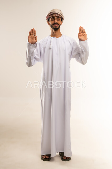 طلب التوقف وعدم الاقتراب, مفهوم الرفض والامتناع والانزعاج, ايماءات الحزم والجدية, بورتريه لشاب عربي خليجي عماني يرتدي الدشداشة والكمه يمد يده نحو الأمام مع رفع الكف بتعابير النهي عن فعل امر ما, صورة الجسم بالطول الكامل, خلفية بيضاء