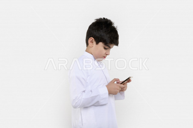 بورتريه لفتى عربي خليجي سعودي مبتسم بيده هاتف محمول ، تسويق إلكتروني ، إستخدام التطبيقات الالكترونية ، ألعاب فيديو ، التعلم عن بعد ، التسوق و الشراء ، خلفية بيضاء