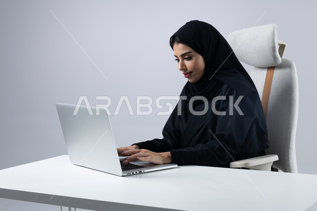 إدارة شؤون الأعمال وتنظيمها, النقر والتفاعل مع لوحة المفاتيح, وضع استراتيجيات وأهداف العمل، بورتريه مقرب لإمرأة عربية سعودية خليجية محجبة ترتدي العباءة تقوم بالعمل على جهاز الحاسب المحمول بإيماءات التركيز والتمعن, خلفية بيضاء