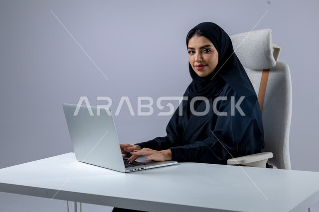 إدارة شؤون الأعمال وتنظيمها, النقر والتفاعل مع لوحة المفاتيح, وضع استراتيجيات وأهداف العمل، بورتريه مقرب لإمرأة عربية سعودية خليجية محجبة ترتدي العباءة تقوم بالعمل على جهاز الحاسب المحمول بإيماءات التركيز والتمعن, خلفية بيضاء