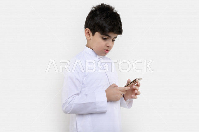 بورتريه لفتى عربي خليجي سعودي مبتسم بيده هاتف محمول ، تسويق إلكتروني ، إستخدام التطبيقات الالكترونية ، ألعاب فيديو ، التعلم عن بعد ، التسوق و الشراء ، خلفية بيضاء