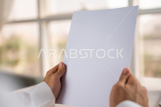 صورة مقربة ليد رجل عربي خليجي سعودي يحمل اوراق خاصة بالعمل، أوراق بيضاء فارغة، سكرتير يدير الاعمال الورقية، أعمال مكتبية