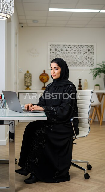  مهن ووظائف نسائية مكتبية سعودية، ادارة وانجاز المهام باستخدام جهاز تقني حديث ومتطور, إمرأة عربية خليجية سعودية مبتسمة ترتدي الحجاب والعباءة تعمل على الحاسوب المحمول في مقر الشركة, ايماءات وتعابير السرور والسعادة