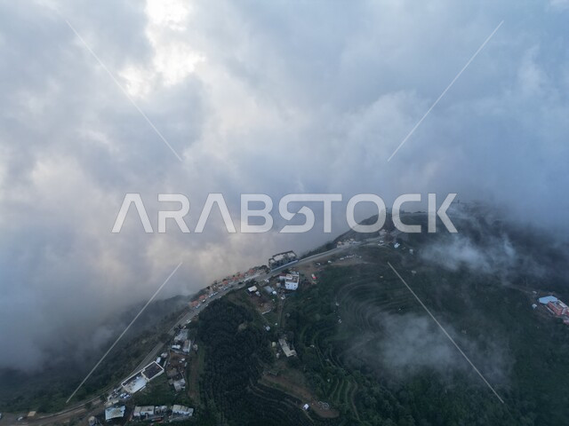 Cloudy sky with white clouds over the mountains of Fifa, natural vegetation on the mountain peaks and heights, green agricultural terraces in Jazan in the Kingdom of Saudi Arabia, natural tourist places and landmarks in Saudi Arabia, nature background