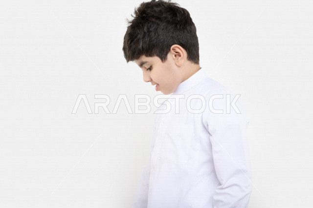 بورتريه لفتى عربي خليجي سعودي مبتسم بينظر إلى أسفل بإيماءات وجه تدل على السعادة ، خلفية بيضاء
