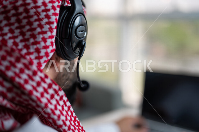 صورة مقربة ليد رجل عربي خليجي سعودي يعمل في خدمة العملاء، موظف يرتدي سماعة الاتصال، استعلامات واستفسارات، الاجابه على اسئلة العملاء، عقد اجتماع عمل عبر الانترنت، العمل عن بعد من خلال الحاسوب المحمول، متابعة وتطوير العمل