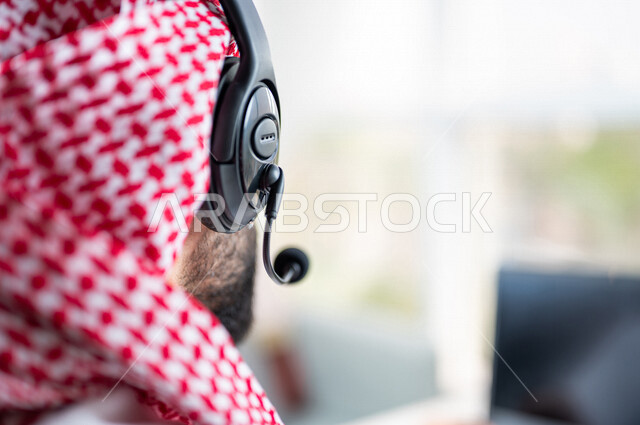 صورة مقربة ليد رجل عربي خليجي سعودي يعمل في خدمة العملاء، موظف يرتدي سماعة الاتصال، استعلامات واستفسارات، الاجابه على اسئلة العملاء، عقد اجتماع عمل عبر الانترنت، العمل عن بعد من خلال الحاسوب المحمول، متابعة وتطوير العمل