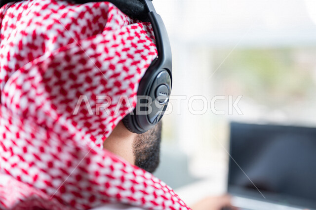 صورة مقربة ليد رجل عربي خليجي سعودي يعمل في خدمة العملاء، موظف يرتدي سماعة الاتصال، استعلامات واستفسارات، الاجابه على اسئلة العملاء، عقد اجتماع عمل عبر الانترنت، العمل عن بعد من خلال الحاسوب المحمول، متابعة وتطوير العمل