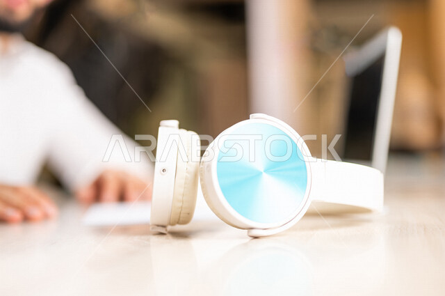 Close-up of the hand of a Saudi Arabian Gulf man using a laptop computer with a wireless headset next to it, listening to electronic courses, listening to music, using modern technologies