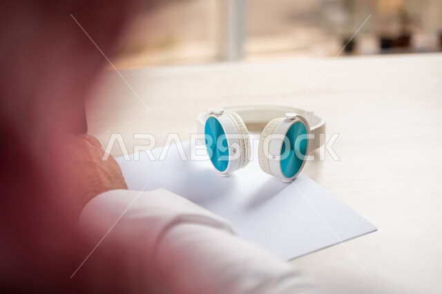 صورة مقربة ليد رجل عربي خليجي سعودي يستخدم الحاسوب المحمول وبجانبه سماعة لاسلكية، الاستماع الى الدورات الالكترونية، الاستماع الى الموسيقى، استخدام تقنيات حديثة
