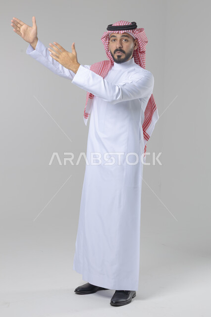 الإشارة إلى شيء ما, الوقوف باستقامة واعتدال, تعابير وايماءات السرور والسعادة، بورتريه لرجل عربي خليجي سعودي يرتدي الثوب التقليدي و الشماغ يشير بيديه لمكان معين, صورة للجسم بالطول الكامل, خلفية بيضاء