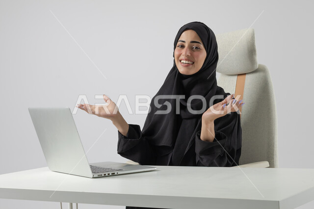  مهن ووظائف نسائية مكتبية سعودية، ادارة وانجاز المهام باستخدام جهاز تقني حديث ومتطور, بورتريه مقرب إمرأة عربية خليجية سعودية مبتسمة ترتدي الحجاب والعباءة تعمل على الحاسوب المحمول, ايماءات وتعابير السرور والسعادة، خلفية بيضاء