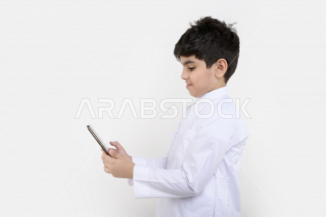 بورتريه لفتى عربي خليجي سعودي مبتسم بيده هاتف محمول ، تسويق إلكتروني ، إستخدام التطبيقات الالكترونية ، ألعاب فيديو ، التعلم عن بعد ، التسوق و الشراء ، خلفية بيضاء