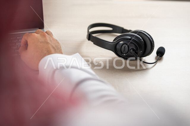 صورة مقربة ليد رجل عربي خليجي سعودي يعمل في خدمة العملاء، استعلامات واستفسارات، الاجابه على اسئلة العملاء، عقد اجتماع عمل عبر الانترنت، العمل عن بعد من خلال الحاسوب المحمول، متابعة وتطوير العمل