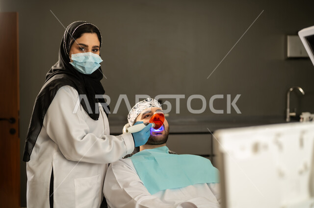 جراحة الفم والأسنان، تقديم الخدمات الصحية في المراكز التخصصية، إجراء الفحوصات الطبيه ، شاب عربي خليجي سعودي يرتدي الزي التقليدي يجلس في العيادة السنية ويفتح فمه لتشخيص المرض, صورة مقربة ليد طبيبة عربية خليجيه سعودية ترتدي القفازات والكمامة الطبية تقوم بفحص أسنان المريض ، شاب عماني يجلس على كرسي العلاج .