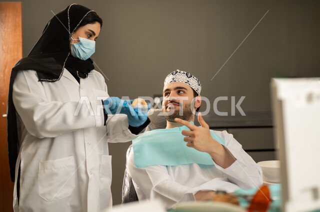 معالجة التسوس و النخر, استخدام الادوات اللازمة لإجراء الفحوصات الطبيه ,شاب عربي خليجي سعودي يرتدي الزي التقليدي يجلس في العيادة السنية ويفتح فمه لتشخيص المرض, صورة مقربة لطبيبة عربية خليجيه سعودية ترتدي القفازات والكمامة الطبية تقوم بفحص أسنان المريض ، شاب عماني على كرسي العلاج .
