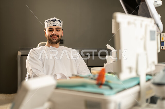 النظر الى الكاميرا بايماءات السعادة ، مفهوم الطب والرعاية الصحية ، تقديم الخدمات والاستشارات الطبية للمراجعين، تدوين معلومات عن حالة المريض، طبي عماني يرتدي الدشداشة والكمة، مهن ووظائف طبية ، الاهتمام والعناية بالمرضي .