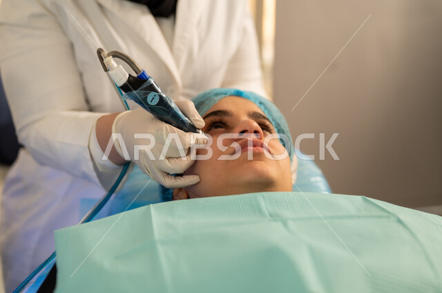 إستخدام مستحضرات مواد التجميل ،عيادة تجميلية نسائية ، خبيرة تجميل تقوم بعمل جلسات العناية بالبشرة ، صورة مقربة لامرأة عربية خليجية سعودية في صالون تجميلي نسائي بايماءات الاسترخاء، مفهوم الأنوثة والنعومة، الاهتمام بتحسين البشرة، امرأة عمانية تهتم بروتين التقشير والتفتيح والتدليك .