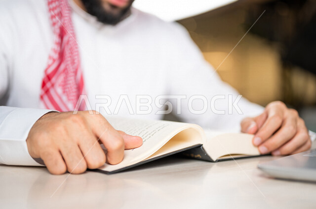 A close-up of a Saudi Arabian Gulf man reading a book, a scientific researcher, a university book, stories and novels, knowledge acquisition, education and culture