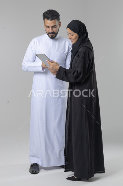 تبادل الأفكار والخبرات لتحقيق أهداف الشركة، العمل الجماعي وروح الفريق الواحد، بورتريه لزميلين عربيين سعوديين خليجيين يقومان بمناقشة و تنظيم الاعمال بإستخدام جهاز التابليت، دمج العمل مع التقنية والتكنولوجيا، صورة الجسم بالطول الكامل، خلفية بيضاء