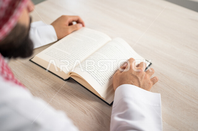 صورة مقربة لرجل عربي خليجي سعودي يقرا الكتاب، باحث علمي، كتاب جامعي، قصص وروايات، اكتساب المعرفة، تعليم وثقافة