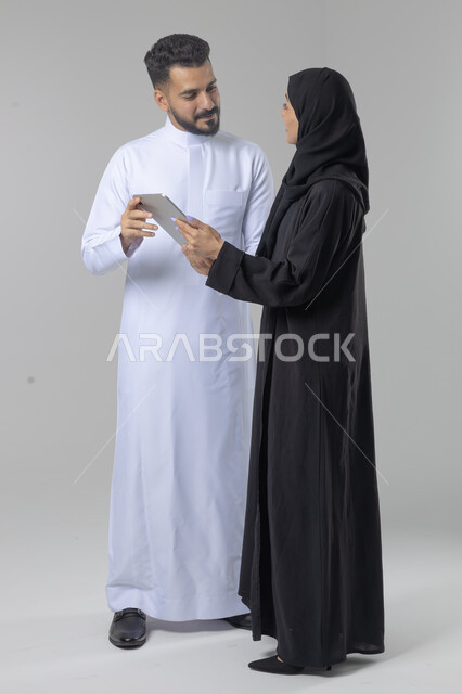 تبادل الأفكار والخبرات لتحقيق أهداف الشركة، العمل الجماعي وروح الفريق الواحد، بورتريه لزميلين عربيين سعوديين خليجيين يقومان بمناقشة و تنظيم الاعمال بإستخدام جهاز التابليت، دمج العمل مع التقنية والتكنولوجيا، صورة الجسم بالطول الكامل، خلفية بيضاء