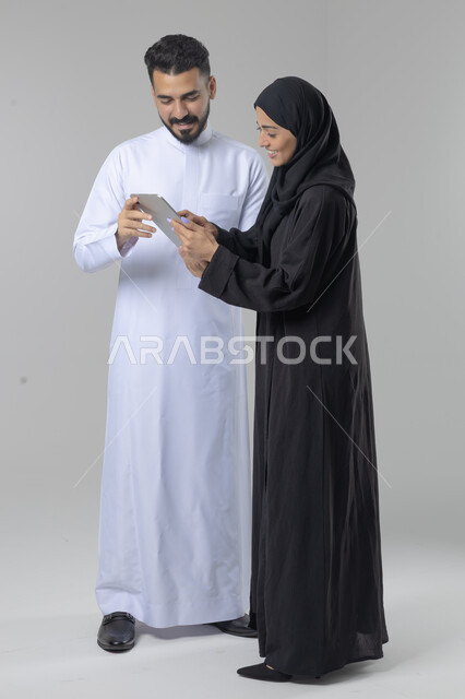 تبادل الأفكار والخبرات لتحقيق أهداف الشركة، العمل الجماعي وروح الفريق الواحد، بورتريه لزميلين عربيين سعوديين خليجيين يقومان بمناقشة و تنظيم الاعمال بإستخدام جهاز التابليت، دمج العمل مع التقنية والتكنولوجيا، صورة الجسم بالطول الكامل، خلفية بيضاء